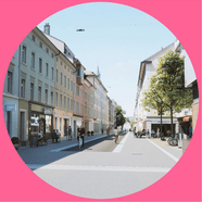 Strassenszene mit Fussgängern und Fahrrädern, flankiert von Gebäuden.
