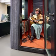 Person spielt Akustikgitarre in einer schallisolierten Kabine.