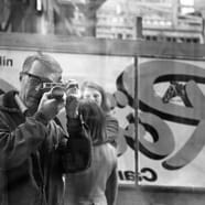 Schwarzweissfoto einer Person mit Kamera, reflektiert im Schaufenster.