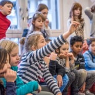 Kinder sitzen und heben die Hand in einem Raum.