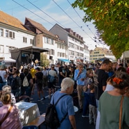 Menschenmenge auf einem Strassenfest mit Bühne und Ständen.
