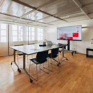 Moderner Konferenzraum mit Tisch, Stühlen und grossem Bildschirm.