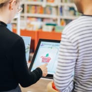 Zwei Personen an einem Selbstbedienungsterminal in einer Bibliothek.