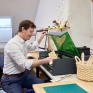 Person in weissem Hemd arbeitet an einem Tisch mit einem Laser Cutter.