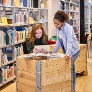 Zwei Personen in einer Bibliothek, die ein Tablet betrachten.