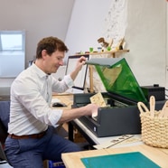 Person in weissem Hemd arbeitet an einem Tisch mit einem Laser Cutter.