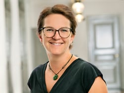 Person mit Brille lächelt in einem Innenraum.