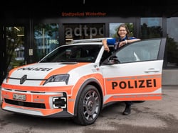 Polizeiauto vor einem Gebäude mit einer Person in Uniform an der Autotür.