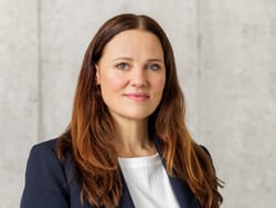 Person mit langen Haaren und Blazer vor neutralem Hintergrund.