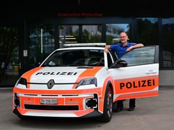 Person neben einem Polizeiauto vor einem Gebäude.