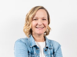Person mit blonden Haaren in blauer Jeansjacke vor weissem Hintergrund.