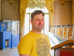 Mann im gelben Hemd steht in elegantem Raum mit Ausstellungsstücken.