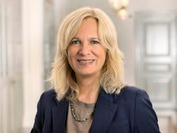 Frau mit blonder Frisur in Geschäftskleidung.
