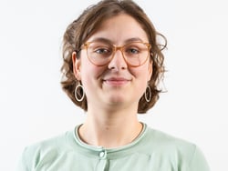 Person mit Brille und Ohrringen vor weissem Hintergrund.