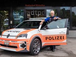 Person steht neben einem Polizeiauto vor einem Gebäude.