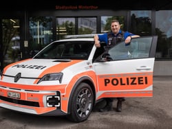 Polizist steht neben einem Polizeiauto mit geöffneter Tür.