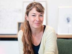 Person mit langem Haar sitzt auf einem Stuhl und lächelt.