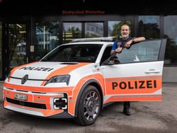 Eine Person steht neben einem Polizeiauto vor einem Gebäude.