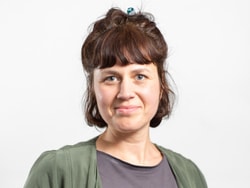 Frau mit dunklen Haaren und grünem Oberteil vor weissem Hintergrund.