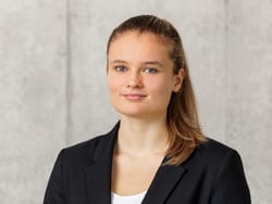 Person mit schwarzem Blazer vor grauem Hintergrund.