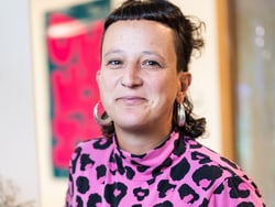Person mit rosa Leopardenmuster-Oberteil und Ohrringen vor Kunstwerk.