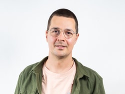 Mann mit Brille und grünem Hemd vor weissem Hintergrund.