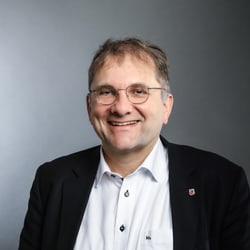 Stefan Fritschi in Anzug vor grauem Hintergrund.