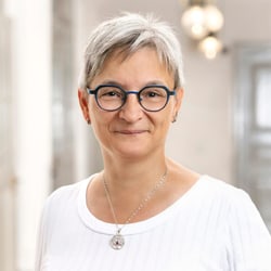 Person mit Brille und kurzem grauem Haar lächelt in heller Umgebung.