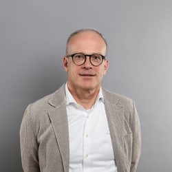 Mann mit Brille und Jackett vor grauem Hintergrund.