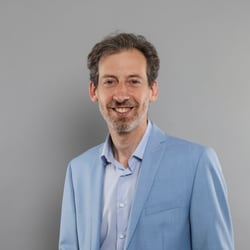 Mann in blauem Anzug vor grauem Hintergrund.