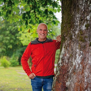 Person in roter Jacke lehnt an einem Baum im Park.
