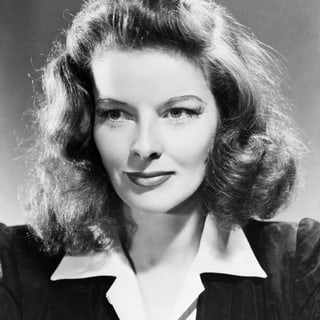 Schwarzweiss-Porträt von Katharine Hepburn. Sie trägt darauf wellige offene Haare, eine weisse Hemdbluse und eine Blazer.