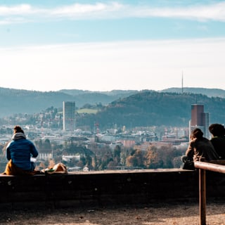 Menschen sitzen auf einer Mauer mit Stadtblick im Hintergrund.