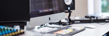 Tisch mit Computer, Musiksoftware auf Monitor, Lautsprecher und Audioausrüstung.