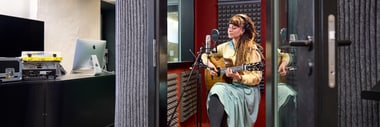 Person spielt Akustikgitarre in einer schallisolierten Kabine.
