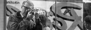 Schwarzweissfoto einer Person mit Kamera, reflektiert im Schaufenster.