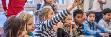 Kinder sitzen und heben die Hand in einem Raum.