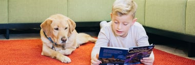 Ein Junge liest neben einem Lesehund.