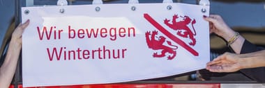 Drei Personen halten eine Blache mit rotem Text und Winterthur Wappen.