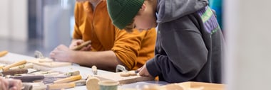 Zwei Personen schnitzen an einem Tisch.