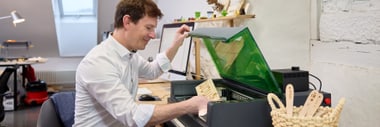Person in weissem Hemd arbeitet an einem Tisch mit einem Laser Cutter.