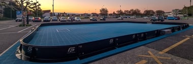 Feldhockeyplatz mit Autos im Hintergrund bei Sonnenuntergang.
