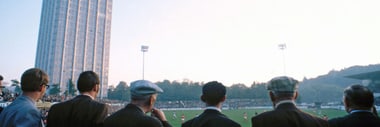 Männer stehen im Vordergrund, blicken auf das Sportstadion Schützenwiese bei Sonnenuntergang.