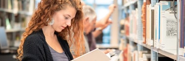 Person mit lockigem Haar liest Buch in Bibliothek.