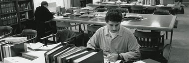 Menschen in einer Bibliothek mit Tischen voller Bücher.