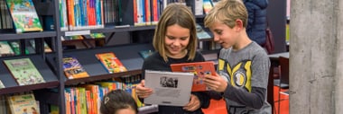 Drei Kinder blättern in Büchern in einer Bibliothek.