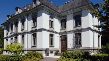 Historisches städtisches Gewerbegebäude mit weissen Wänden und dunklem Dach.