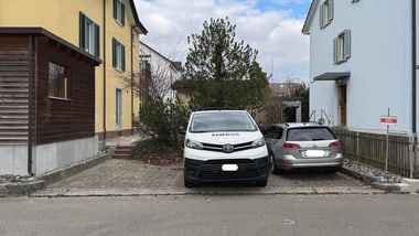 Zwei geparkte Autos zwischen Gebäuden auf einem Parkplatz.