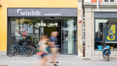 Aussenansicht der Stadtbibliothek mit gehenden Personen.
