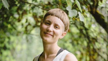 Lyn Bentschik in weisser Kleidung im Garten mit Bäumen.
